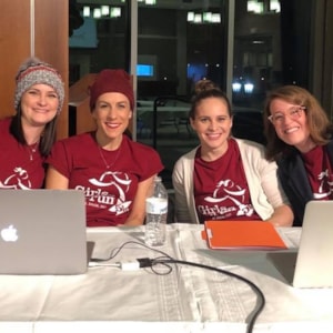 4 women in red Girls on the Run shirts sit at a table while helping at an event